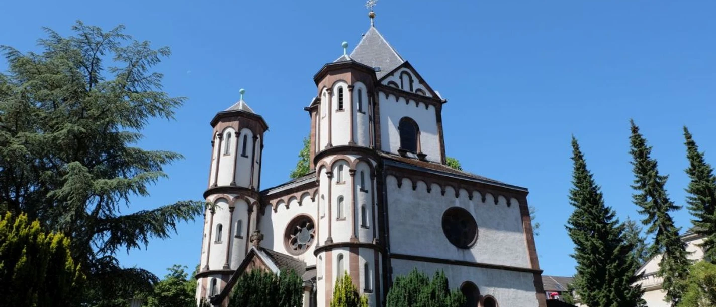 Marienkapelle Burtscheid Romanische Marienkapelle mit weißem Mauerwerk und kunstvollen Türmen, von Grün umgeben.