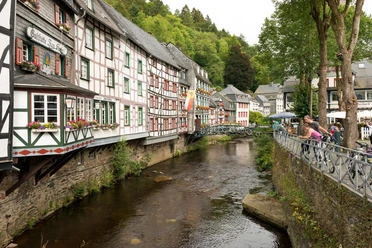 Traditionelle Fachwerkhäuser entlang eines Flusslaufs mit blühenden Blumenkästen an den Fenstern.
