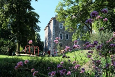 Burg Frankenberg Burg Frankenberg umgeben von grünen Bäumen und violetten Blumen im Vordergrund.