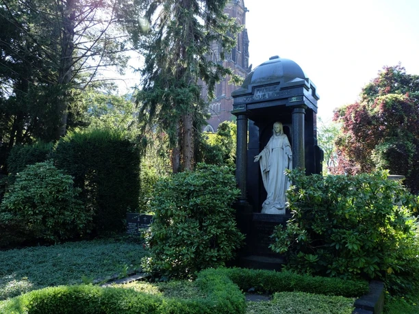 Grabstätten umgeben von grünen Bäumen und Sträuchern im Sonnenlicht.
