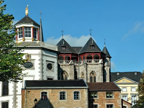Fassade von einer Kirche mit gotischen Elementen und einem achteckigen, rot und gold verzierten Turm.