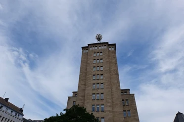 Auf einem hohen, turmähnlichen Gebäude mit Fenstern steht eine Wetterstation mit runder Kuppel unter leicht bewölktem Himmel..