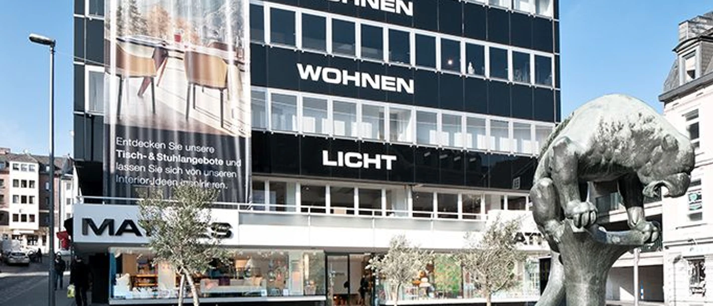 Mathes Modernes, mehrstöckiges Gebäude mit der Skulptur des Bahkauvs im Vordergrund. An den einzelnen Etagen des Gebäudes steht "LICHT", darüber "WOHNEN", darüber "WOHNEN" und ganz oben "OFFICE".