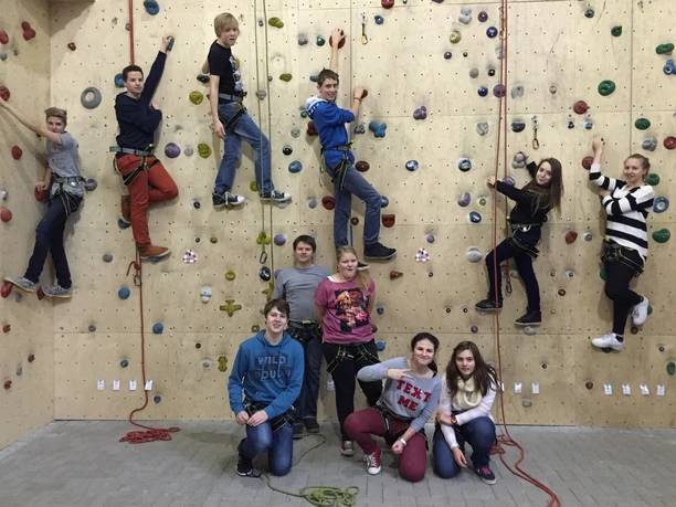Kletterhalle Abenteuerzeit Kinder und Jugendliche klettern gemeinsam an einer bunten Kletterwand in einer Sporthalle.