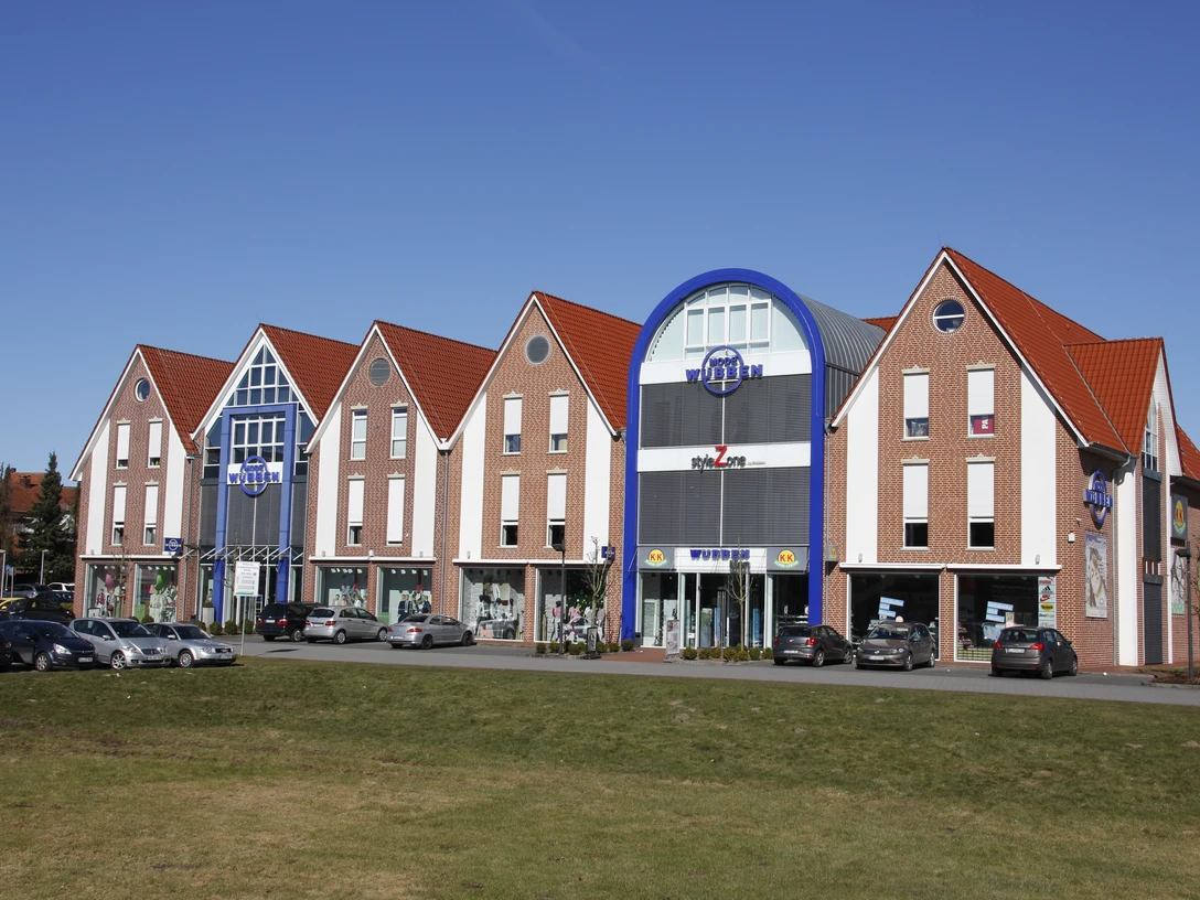 Mode Wübben Backsteinfassade mit roten Giebeldächern und blauer Eingangsfassade des Modehauses Wübben in Haselünne