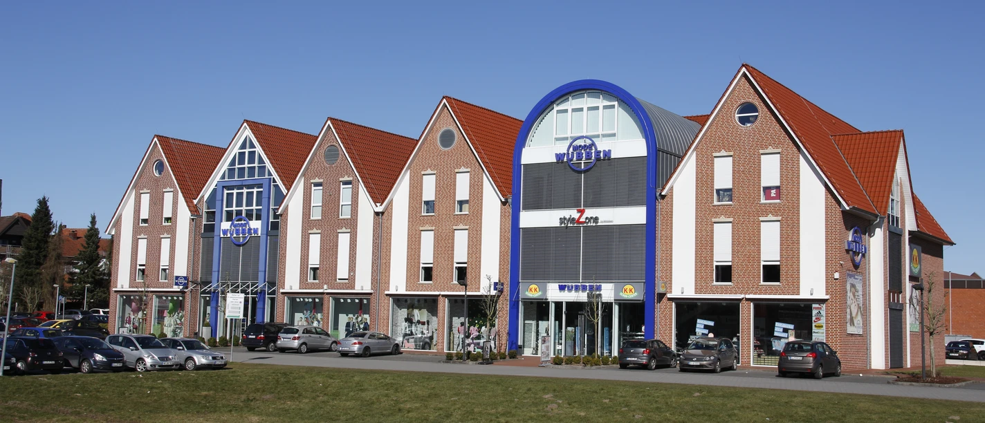 Mode Wübben Backsteinfassade mit roten Giebeldächern und blauer Eingangsfassade des Modehauses Wübben in Haselünne