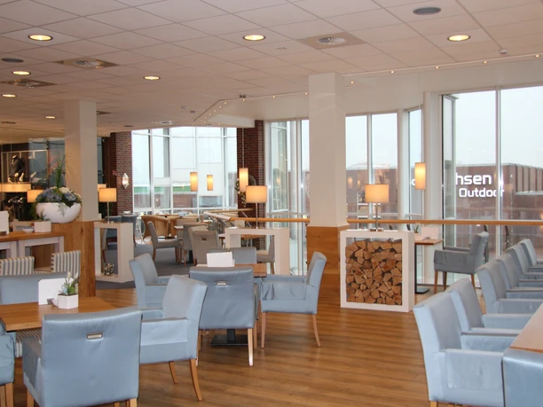 Klahsen Heller Sitzbereich mit großen Fenstern, blauen Polsterstühlen, Holzboden und modernen Lampen.