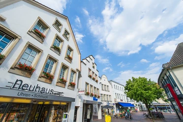 Fußgängerzone in Lingen mit weißen Giebelhäusern, Blumenkästen und Geschäften unter blauem Himmel.