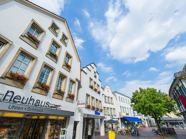 Innenstadt Lingen Fußgängerzone in Lingen mit weißen Giebelhäusern, Blumenkästen und Geschäften unter blauem Himmel.