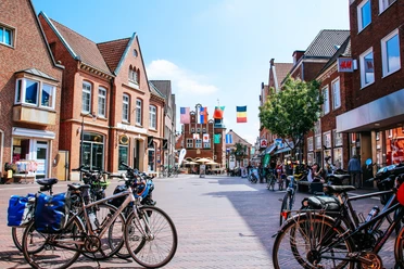 Innendstadt Meppen Belebte Einkaufsstraße in Meppen mit roten Backsteinhäusern, Fahrrädern und Fahnen über dem Platz.