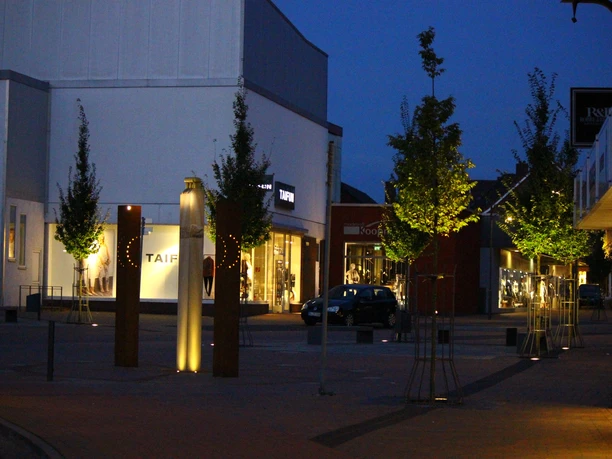 Innenstadt Werlte Abendliche Einkaufsstraße in Werlte mit beleuchteten Schaufenstern, jungen Bäumen und moderner Beleuchtung.