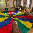 Kinder und Erwachsene sitzen im Kreis und spielen gemeinsam mit einem großen bunten Schwungtuch.