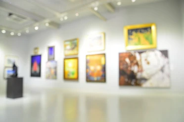 Moderne Galerie mit hellen Wänden, an denen diverse, bunte Gemälde hängen.