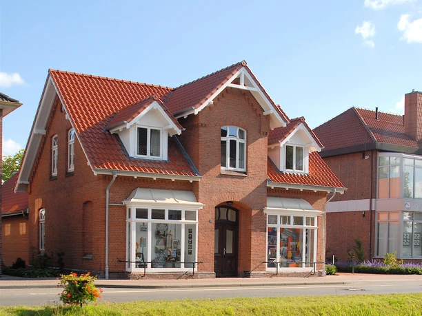 Haus der Kultur, Fehntjer Forum, Rhauderfehn Ein großes Backsteinhaus mit einem roten Dach und weißen Fensterrahmen an einer Straße und einem Kanal.
