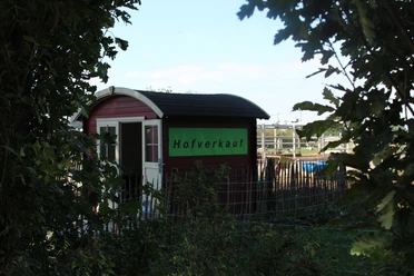 Engelnhof Kleiner roter Verkaufshaus mit grünem Schild „Hofverkauf“, eingerahmt von Bäumen und Weidezaun.