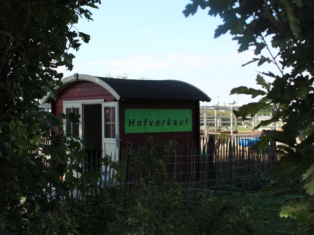 Engelnhof Kleiner roter Verkaufshaus mit grünem Schild „Hofverkauf“, eingerahmt von Bäumen und Weidezaun.
