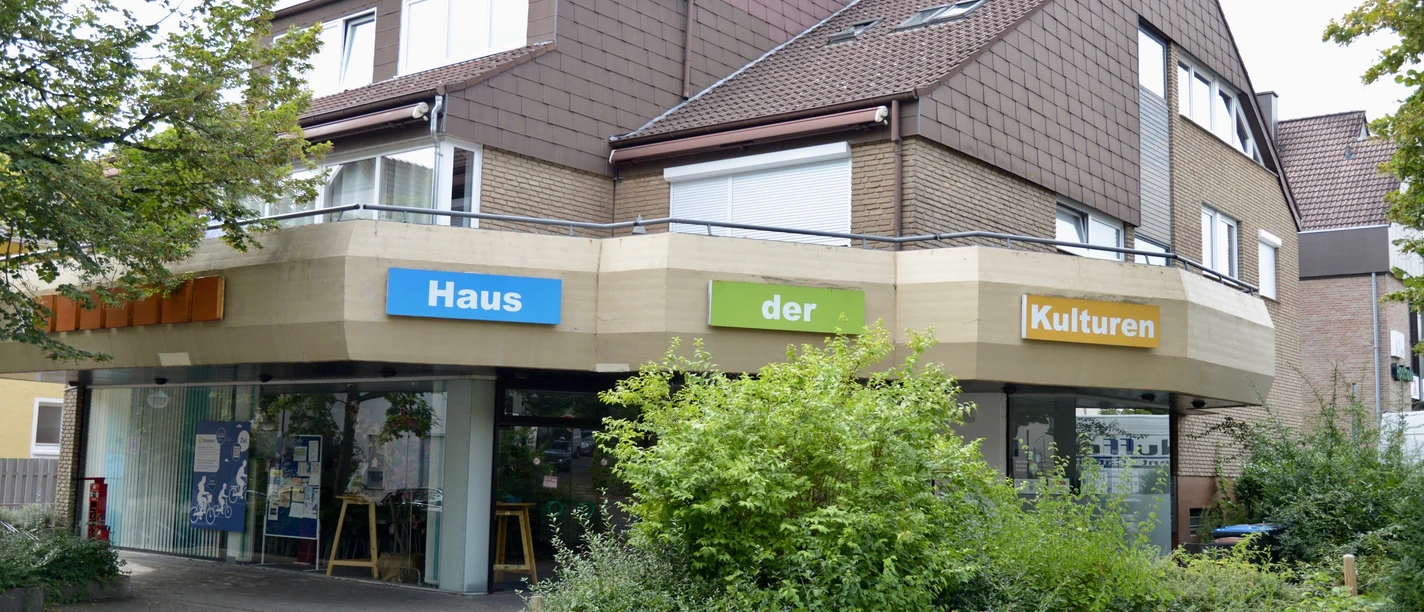 Modernes Gebäude mit Schriftzug "Haus der Kulturen", umgeben von Bäumen und Pflanzen.
