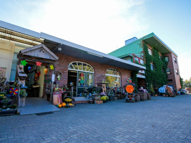 Torf- und Erdenhof Lammers Eingangsbereich eines Hofladens mit Backsteinfassade, Pflanzen, Dekorationen und bunten Windrädern