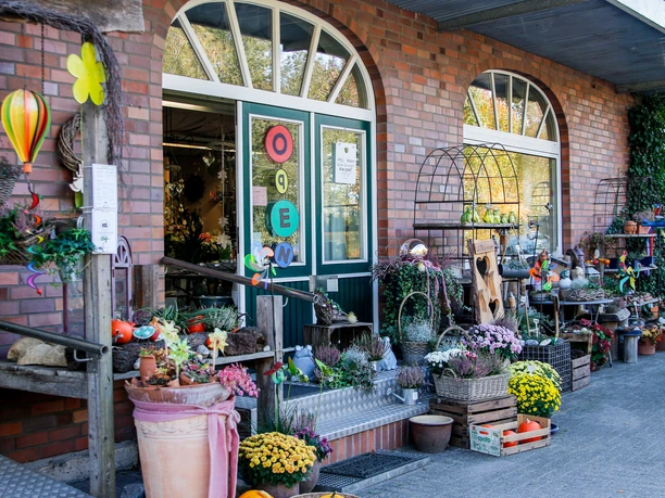 Torf- und Erdenhof Lammers Eingang eines Hofladens mit bunten Blumen, Pflanzen, Dekoartikeln und einem offenen Verkaufsschild.