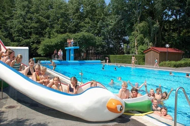 Freibad Lathen Kinder und Erwachsene genießen das Schwimmen und Rutschen im Freibad mit großer blauer Beckenanlage.