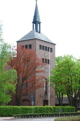 St.-Marien-Kirche in Rastdorf Backsteinkirche mit hohem Turm und spitzem Dach, umgeben von grünen und roten Bäumen.