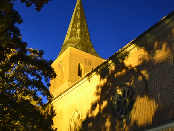 St.-Sixtus-Kirche in Werlte Backsteinkirche mit hohem Turm und spitzem Dach, angestrahlt im warmen Licht einer klaren Nacht