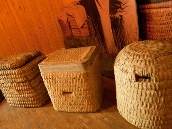 bienenkoerbe-bienenwelten Drei handgefertigte Bienenkörbe aus Stroh auf Holzboden im warmen Licht eines Holzraums.