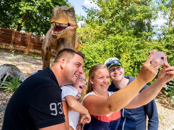 serengeti-park-jurassic-safari Familie macht Selfie vor lebensgroßer Dinosaurierfigur in der Jurassic-Safari des Serengeti-Parks Hodenhagen.