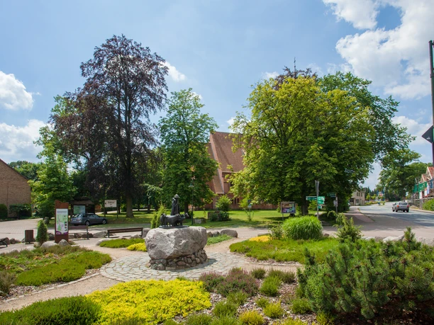bispingen-ortsmitte Die örtliche Beschreibung des Bildes von der Bispinger Ortsmitte könnte wie folgt aussehen:Ein malerischer Platz in der Ortsmitte von Bispingen mit gepflegten Grünflächen, Bänken und einem großen Baum. Im Vordergrund ist eine steinerne Skulptur zu sehen, während im Hintergrund bunte Gebäude den Charme des Dorfes unterstreichen.