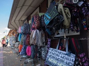 bispinger-kleiner-speicher-außen Das Bild zeigt eine Außenansicht eines Ladengeschäftes in Bispingen. Vor dem Geschäft sind bunte Handtaschen und Rucksäcke ausgestellt, die an Gestellen hängen oder auf kleinen Tischen präsentiert werden. Personen schlendern entspannt auf dem gepflasterten Gehweg neben der Auslage entlang.The picture shows an exterior view of a store in Bispingen. Colorful handbags and backpacks are displayed in front of the store, hanging on racks or presented on small tables. People stroll relaxed along the paved sidewalk next to the display.Billedet viser et udvendigt billede af en butik i Bispingen. Farverige håndtasker og rygsække er udstillet foran butikken, hængende på stativer eller præsenteret på små borde. Folk slentrer langs det brostensbelagte fortov ved siden af udstillingen.De foto toont een buitenaanzicht van een winkel in Bispingen. Kleurrijke handtassen en rugzakken worden voor de winkel uitgestald, hangend aan rekken of gepresenteerd op kleine tafeltjes. Mensen wandelen over de geplaveide stoep naast de uitstalling.