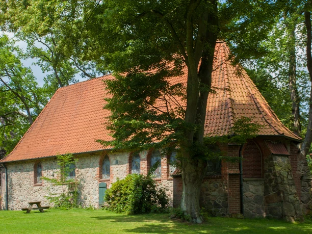 bispingen-ole-kerk Die alte Kirche in Bispingen aus Feld- und Backsteinen mit rotgedecktem Satteldach, umgeben von Grün.