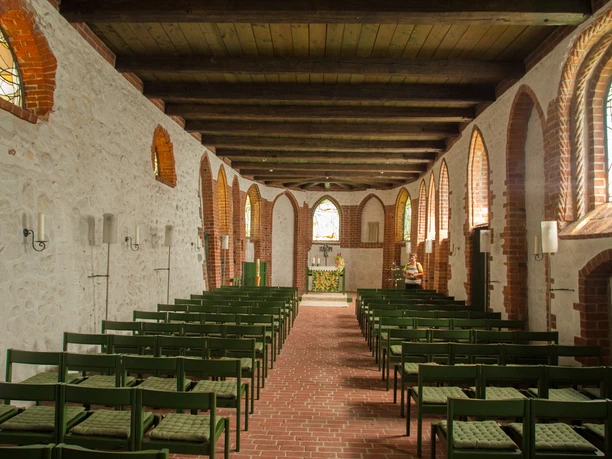 bispingen-kirche-innenraum Die Bispingen Kirche im Inneren zeigt eine Reihe von Holzbänken, umgeben von leuchtenden Buntglasfenstern und einem von Holzdeckenbalken überspannten Raum, der einen warmen, einladenden Charakter verleiht.