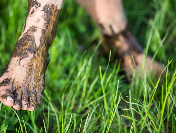fuss-barfusspark-gras Ein nackter Fuß steht im grünen Gras, bedeckt mit natürlichem, heilendem Moor.