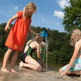 brunausee-schwimmen Eine Gruppe von Kindern spielt fröhlich am Strand, während ein Mädchen mit rotem Kleid Wasser gießt.