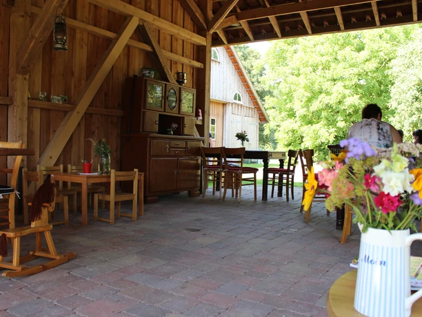 A rustic, covered seating area with wooden furniture and a colorful bouquet of flowers in a white-and-blue-striped vase in the foreground