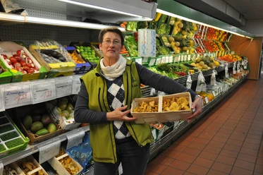 Gemüse- und Bauernmarkt Lüske Verkäuferin im Gemüsemarkt hält frische Pfifferlinge vor einer Auslage mit Obst und Gemüse.