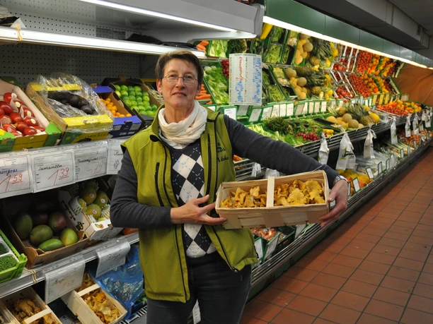 Gemüse- und Bauernmarkt Lüske Verkäuferin im Gemüsemarkt hält frische Pfifferlinge vor einer Auslage mit Obst und Gemüse.