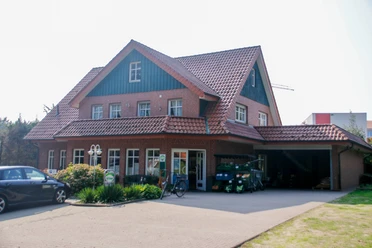 Brümmers Hofladen Backsteingebäude mit Satteldach, Hofladen im Erdgeschoss, davor geparkte Autos und Obststände.