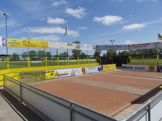 Murmelarena in Uttum Sandige Spielfläche der Murmelarena mit Werbebanden neben einem grünen Sportplatz.