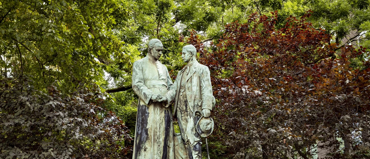 Adolf Kolping Monument Adolf Kolping monument, consisting of two respectfully designed bronze statues, surrounded by lush trees.