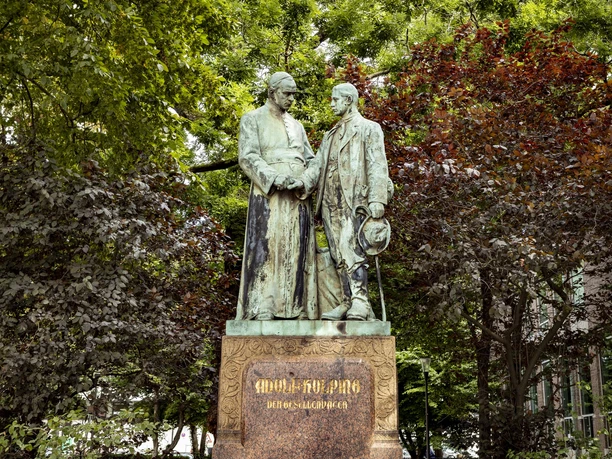 Adolf Kolping Monument Adolf Kolping monument, consisting of two respectfully designed bronze statues, surrounded by lush trees.