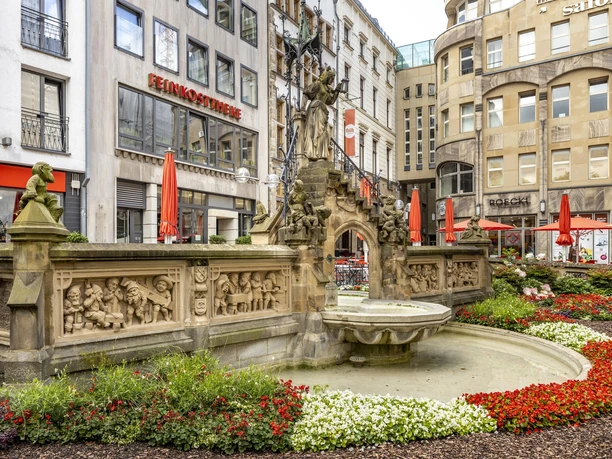 Heinzelmaennchenbrunnen Ein kunstvoller Brunnen mit Skulpturen inmitten urbaner Umgebung.