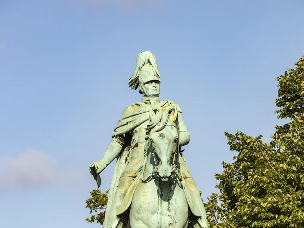 Reiterstandbild König Friedrich Wilhelm IV. Das bronzene Reiterstandbild zeigt König Friedrich Wilhelm IV. von Preußen hoch zu Ross. Es thront imposant auf einem soliden Steinsockel. Dichtes Laub umrahmt die Statue, die bei klarem Himmel eindrucksvoll strahlt.