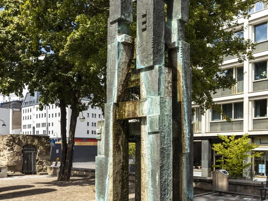 Theo Burauen Fountain Der Theo-Burauen-Brunnen in Köln zeigt eine moderne, bronzene Skulptur mit gestapelten Blöcken.The Theo Burauen Fountain in Cologne features a modern, bronze sculpture with stacked blocks.