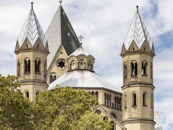 Saint Apostles Das Bild zeigt die romanische Sankt Aposteln in Köln. Ihre markanten Türme erheben sich über die grünen Baumkronen, während der Himmel im Hintergrund von sanften Wolken überzogen ist.The picture shows the Romanesque Sankt Aposteln in Cologne. Its striking towers rise above the green treetops, while the sky in the background is covered in soft clouds.
