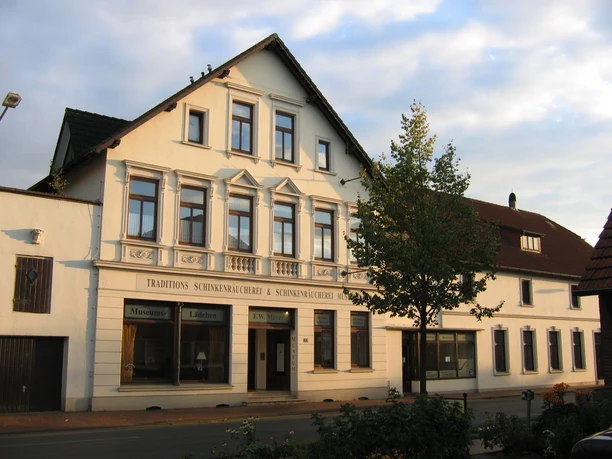 Schinkenmuseum-Apen Das Bild zeigt ein traditionelles Gebäude mit einem Schild, das "Traditions-Schinkenräucherei & Schinkenmuseum" anzeigt.