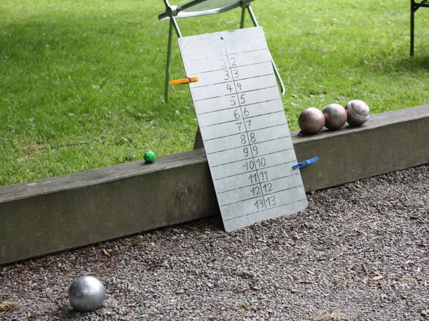 Boulesplatz Organisierte Boulespielanlage im Freien mit Punktetafel auf Kiesboden und Boulekugeln auf Holzbalken.