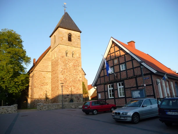 Evangelisch-reformierte Kirche in Lengerich Steinkirche mit hohem Turm und Fachwerkhaus daneben unter blauem Himmel im Abendlicht.