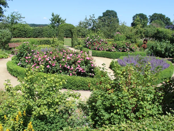 Bauerngarten Lorup Blühende Beete mit Rosen und Lavendel, umrahmt von Buchshecken und geschwungenen Gartenwegen.