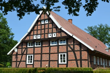 Heimathaus Vrees Historisches Fachwerkhaus mit rotem Ziegeldach, weißen Fensterrahmen und grünem Umfeld.